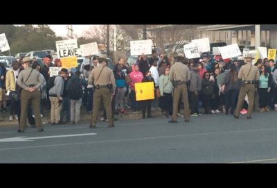 Group of protesters hold up signs while MD State Troops observe the crowd